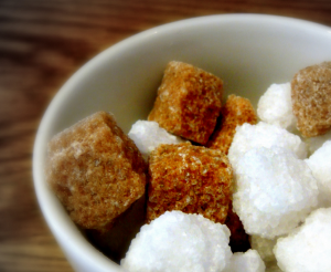 How many grams of natural sugar per day? White and borwn sugar cubes in a white bowl on a brown table.