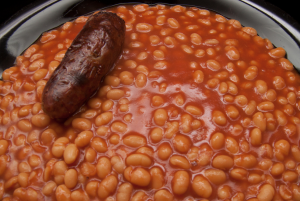 Baked Beans Benefits, baked beans cooking in a pan with a sausage.